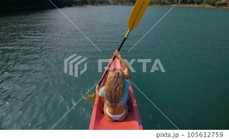 Seductive blonde woman in blue swimsuit sails on pink plastic kayak along azure sea at exotic resort backside upper above view. 105612759