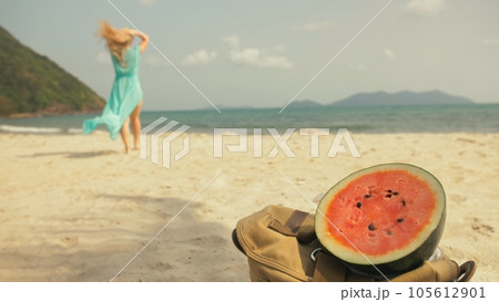The cheerful woman in blur, against the background of a watermelon on tropical sand beach sea. Portrait attractive girl spend summer weekend. 105612901