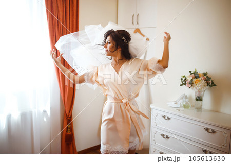 Elegant bride in white robe posing under curtain. Amazing bride in the morning preparation. Elegant bride in white robe posing under curtain. Amazing bride in the morning preparation. 105613630