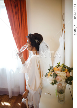 Elegant bride in white robe posing under curtain. Amazing bride in the morning preparation. 105613631