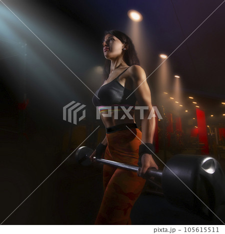 Strong woman doing weights.Sports lifestyle Beautiful fitness woman lifting dumbbells . Fitness sporty woman showing her well trained body. A beautiful girl's body with rippling muscles from strength 105615511