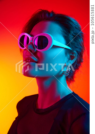 Close up of excited young woman in sunglasses and black transparent top over gradient yellow-red neon background. Close up of excited young woman in sunglasses and black transparent top over gradient yellow-red neon background. 105615881