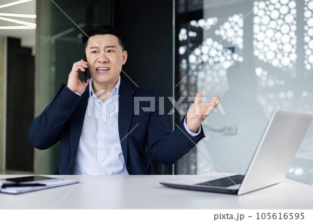 Angry angry asian boss talking on the phone, businessman at workplace shouting into the phone, asian man on interior of office in business suit and investor disappointed. Angry angry asian boss talking on the phone, businessman at workplace shouting into the phone, asian man on interior of office in business suit and investor disappointed. 105616595