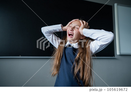 Caucasian girl stands at the blackboard holding her head with her hands. The schoolgirl did not prepare for the lesson.  105619672