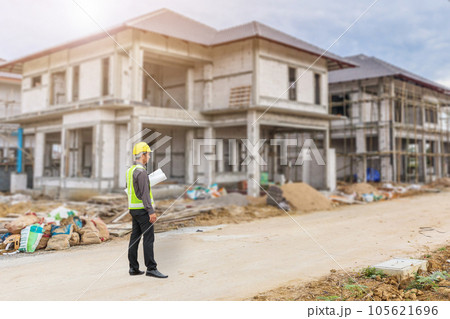 young professional engineer in protective helmet and blueprints paper at the house building construction site 105621696