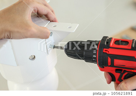 man assembling white table furniture at home using cordless screwdriver 105621891