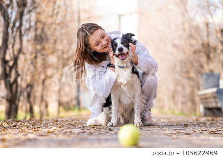 Caucasian woman hugging her dog on a walk in the autumn park. Border collie looks at the ball. 105622969
