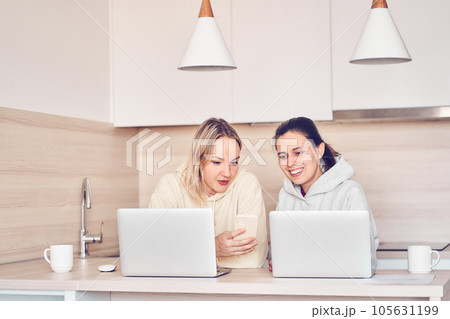 Online training. Two happy women using a laptop, work and study online together or make video calls while sitting at a table. The concept of a career of a female entrepreneur. High quality photo 105631199