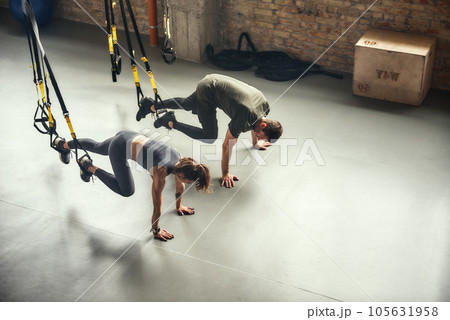 Young and sporty. Top view of a couple in sportswear training with Trx fitness straps at gym 105631958