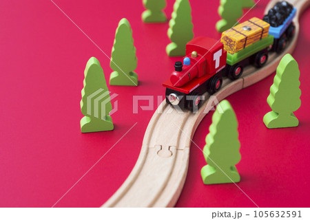 Wooden toy train on the railroad among green trees on red background. Wooden toy train on the railroad among green trees on red background. 105632591