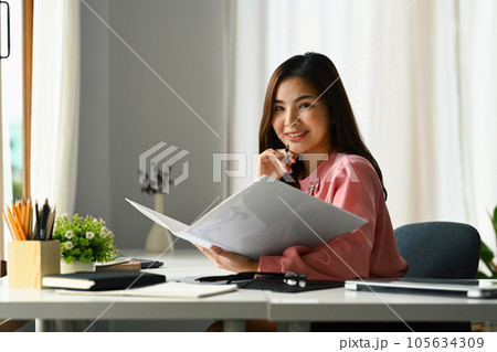 Attractive young female employee sitting at working desk and preparing for negotiations or seminar. Attractive young female employee sitting at working desk and preparing for negotiations or seminar. 105634309