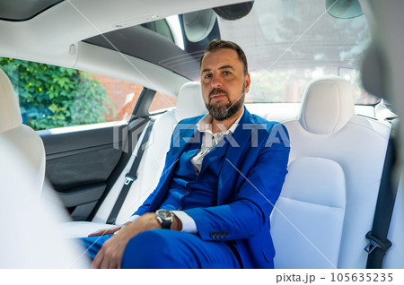 A caucasian man in a blue suit sits in the back seat of a car. Business class passenger. A caucasian man in a blue suit sits in the back seat of a car. Business class passenger. 105635235