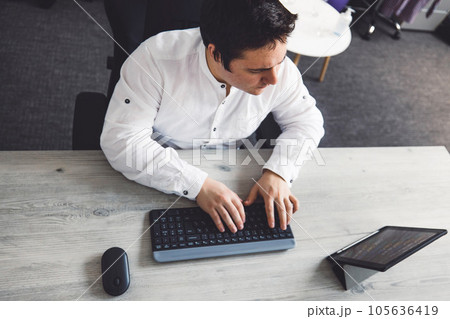 Top down view programmer sitting at his desk in the office typing on a wireless keyboard  105636419