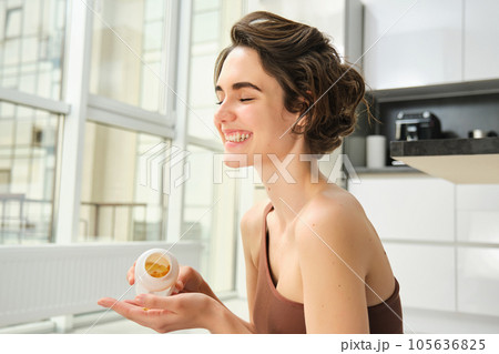 Smiling healthy woman doing sports at home, takes vitamins after workout training session, lifestyle and fitness concept Smiling healthy woman doing sports at home, takes vitamins after workout training session, lifestyle and fitness concept 105636825