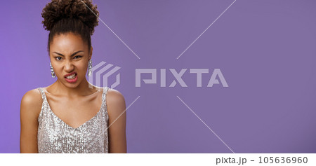 Displeased arrogant african-american woman in silver glittering dress cringing dislike awful smell standing bothered displeased look disgusted frowning standing reluctant blue background 105636960