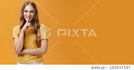 Girl wants keep secret betweet us. Portrait of charming good-looking slim pretty and young woman with long wavy hair and tattoo showing shh gesture with index finger over mouth against orange wall Girl wants keep secret betweet us. Portrait of charming good-looking slim pretty and young woman with long wavy hair and tattoo showing shh gesture with index finger over mouth against orange wall 105637197