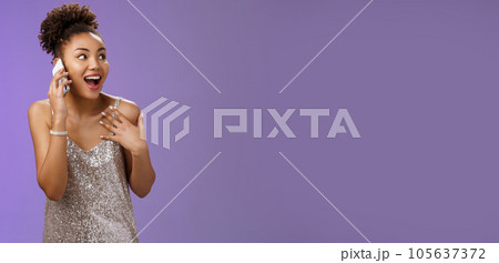 Impressed sociable african-american talkative woman in silver dress talking smartphone pointing herself amused describing emotions impressions after visit awesome party, blue background 105637372