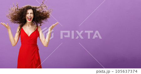 Expressing inner wildness. Portrait of wild and carefree charming european female in stylish evening red dress flicking curly hair up with raised hands laughing out loud enjoying herself during party Expressing inner wildness. Portrait of wild and carefree charming european female in stylish evening red dress flicking curly hair up with raised hands laughing out loud enjoying herself during party 105637374