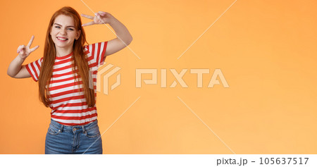 Friendly upbeat good-looking redhead woman rejoicing, feel happy, enjoy summetime, take first photo vacation, send coworkers summer shot, make peace victory signs, smiling broadly orange background 105637517