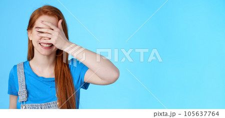 Cheerful tender redhead girlfriend feel happy, enjoy summer holiday, relaxing joyful weekend, playful mood, close eyes hold palm face, hide-n-seek pikaboo gesture, stand blue background 105637764