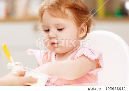 A baby eating yogurt with some on her face. A baby eating yogurt with some on her face. 105638012
