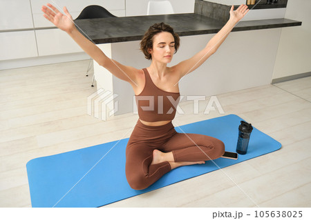 Portrait of fit and healthy woman in sportswear, doing yoga at home on fitness mat, making asana, relaxing and meditating indoors Portrait of fit and healthy woman in sportswear, doing yoga at home on fitness mat, making asana, relaxing and meditating indoors 105638025