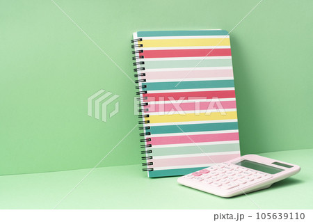 One stripy pastel spiralbound notepad and calculator on green. Back to School or drawing and creativity concept. Copy space. Mockup 105639110