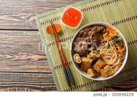 Vietnamese beef noodles salad bun bo xao is filled in fresh herb, savory beef, vegetables and fried spring rolls closeup. Horizontal top view 105640229