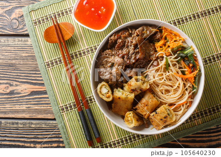 Bun Bo Xao is a Vietnamese noodle salad made with marinated flank steak, vermicelli noodles, vegetables and crispy nem spring rolls closeup. Horizontal top view Bun Bo Xao is a Vietnamese noodle salad made with marinated flank steak, vermicelli noodles, vegetables and crispy nem spring rolls closeup. Horizontal top view 105640230