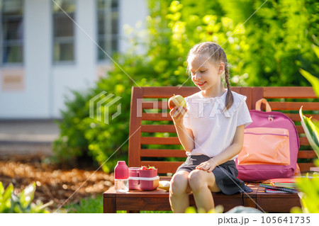 girl is having lunch sitting next to the school 105641735