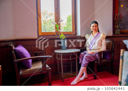 Wide shot of beautiful Asian woman with contemporary Thai dress sit with old furniture in old house Wide shot of beautiful Asian woman with contemporary Thai dress sit with old furniture in old house 105642441