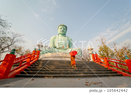 Wide shot side view back of young Asian monk hold red umbrella and walk up on stair in front statue Wide shot side view back of young Asian monk hold red umbrella and walk up on stair in front statue 105642442