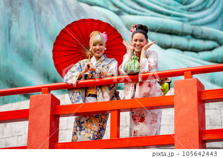 Two Asian pretty women stay close to red railing in the area of base of green big buddha statu Two Asian pretty women stay close to red railing in the area of base of green big buddha statu 105642443