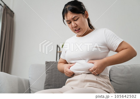 Close up of chubby woman holding her belly fat on the sofa. Diet lifestyle to reduce belly and shape up healthy, abdominal muscle concept. 105642502