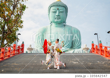 Two Asian young woman with japanese style dress stay on stair in front of green big buddha statue 105642547