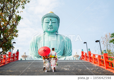 Back of two Asian young woman with japanese style dress walk up on stair to green big buddha statue 105642598