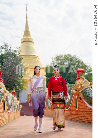 Vertical image of Thai women with traditional dress walk together and discuss on walkway of temple Vertical image of Thai women with traditional dress walk together and discuss on walkway of temple 105642604