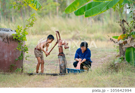 Asian boy help her mother or senior woman to wash pink cloth using underground water 105642994