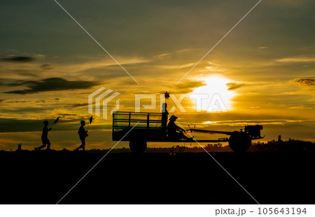 Silhouette of girl hold small windmill and stand on E-taen farm tractor with driver Silhouette of girl hold small windmill and stand on E-taen farm tractor with driver 105643194