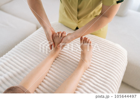 Close-up cropped shot of unrecognizable female masseur doing orthopedic leg exercises of teenager girl client, kneading her ankle, prevention of pain in foot. Concept of medicine children treatment. Close-up cropped shot of unrecognizable female masseur doing orthopedic leg exercises of teenager girl client, kneading her ankle, prevention of pain in foot. Concept of medicine children treatment. 105644497