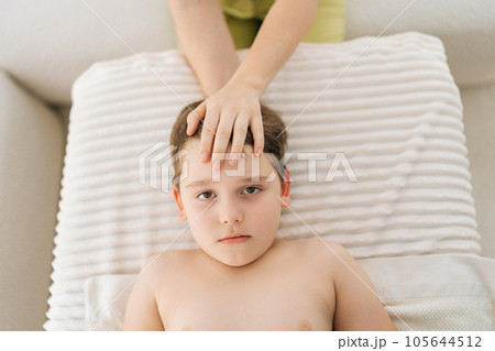 Closeup top view of cute five year old boy laying on bed at manual therapist in osteopath cabinet receiving manual therapy. Professional female physiotherapist adjustment neck, holding head. 105644512