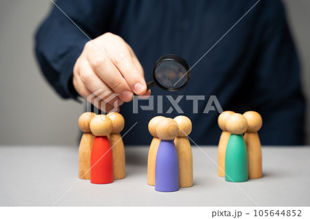 The concept of market segmentation. Target audience, customer care. Market group of buyers. Customer relationship management. Businessman looking through a magnifying glass at figurines of people The concept of market segmentation. Target audience, customer care. Market group of buyers. Customer relationship management. Businessman looking through a magnifying glass at figurines of people 105644852