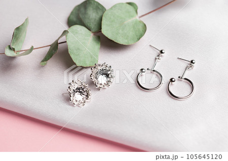 Creative composition with simple silver jewelry earrings set on silk background with dried flowers. Trendy handmade accessories in minimalist style 105645120