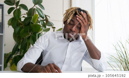 Work fatigue. Exhausted employee. Tired frustrated desperate business man depressed about stress overload sitting at desk in light modern office interior. 105645192