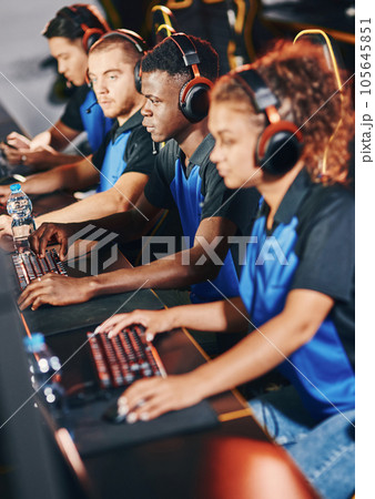 Professional cybersport team wearing headphones participating in eSport tournament, playing online video games while sitting in gaming club or internet cafe Professional cybersport team wearing headphones participating in eSport tournament, playing online video games while sitting in gaming club or internet cafe 105645851