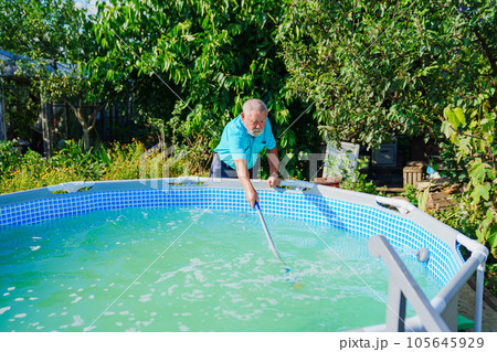 An elderly gray-haired man cleans the walls of the pool with a mop. 105645929