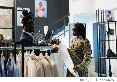 African american woman shopping for pregnancy clothes in modern boutique, worker helping client with the right shirt. Pregnant customer buying fashionable merchandise in clothing store 105646875