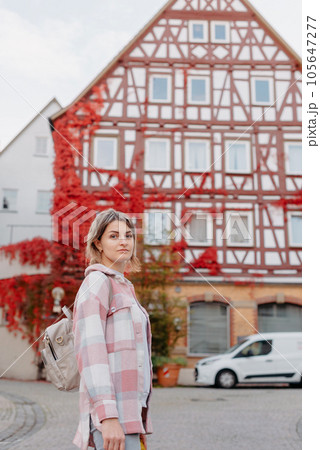 a beautiful girl stands against the background of the window of an old European house, entwined with a floating red color in autumn. Tourism & Travel Concept. Nice portrait of a young woman, in boho 105647277