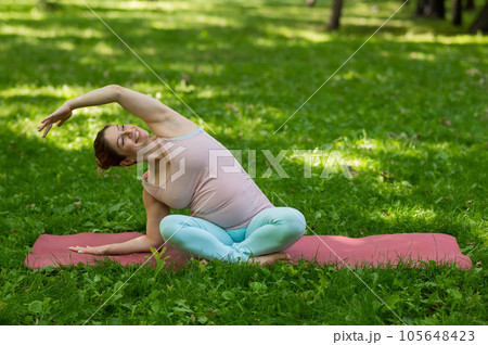 Pregnant caucasian woman doing yoga in the park. Lateral tilt. Pregnant caucasian woman doing yoga in the park. Lateral tilt. 105648423