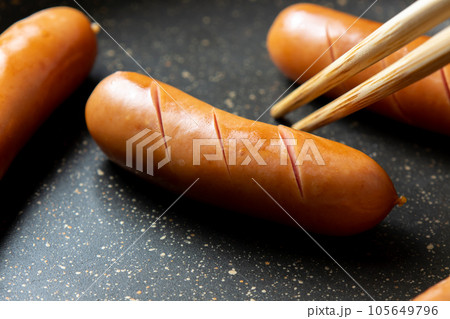 ウインナーソーセージに切れ込みを入れてフライパンで焼く調理シーン。 105649796